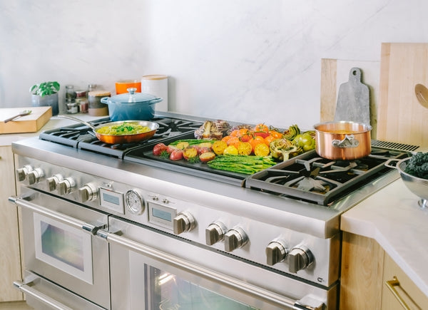 Stainless steel dual fuel range with food cooking on griddle and pots in a modern kitchen setting