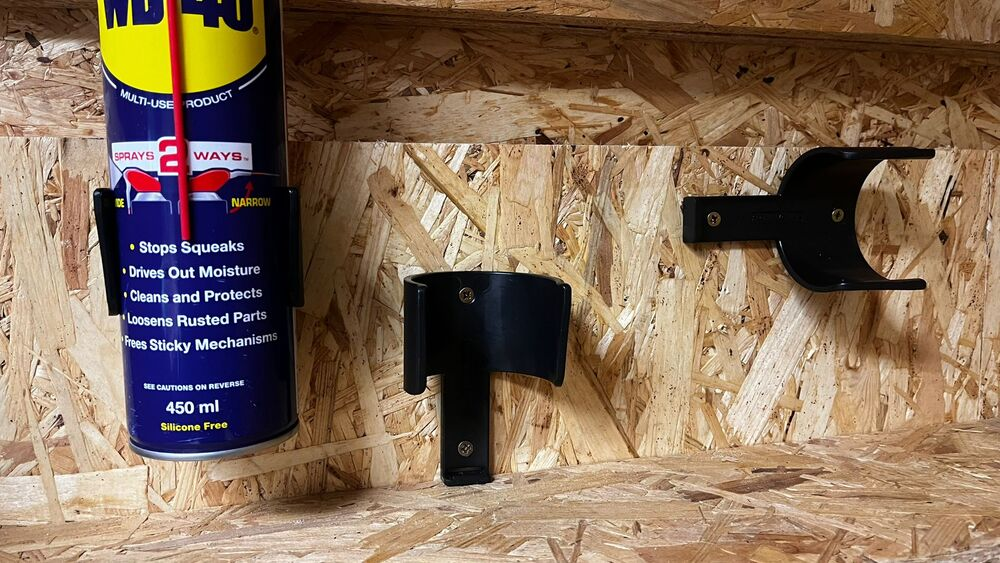 Black metal holders securing spray cans on a wooden garage storage panel for home improvement organization