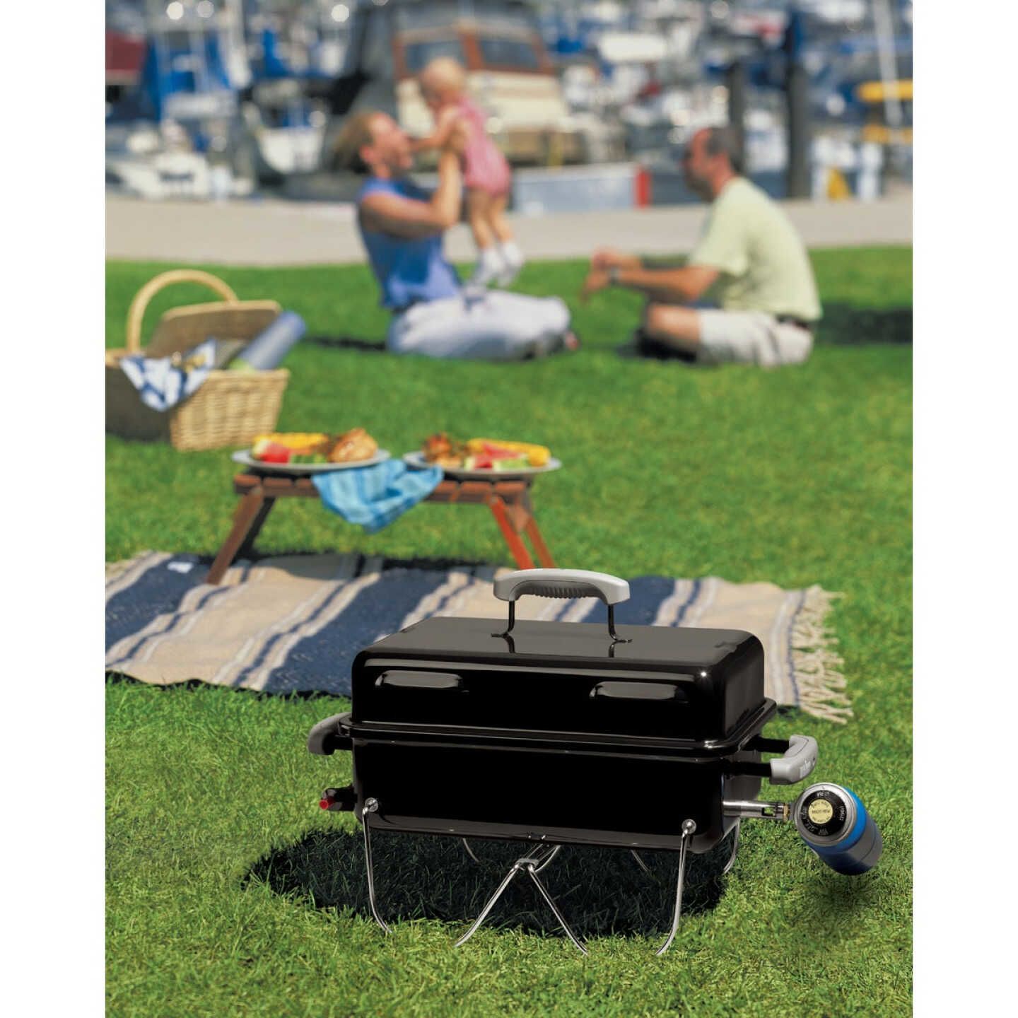 Compact black portable gas grill with single burner and propane canister, set on grass during outdoor picnic and grilling.