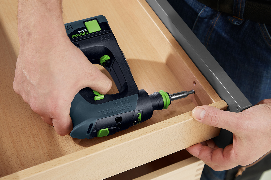 Person using compact Festool cordless drill to fasten screw in light wood drawer in woodworking environment
