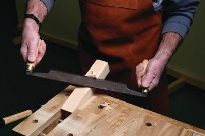 Person using a straight draw knife with wooden handles and steel blade for woodworking in home improvement tasks