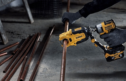 Worker using a DEWALT impact tool with copper pipe cutter attachment for precision cutting in home improvement tasks