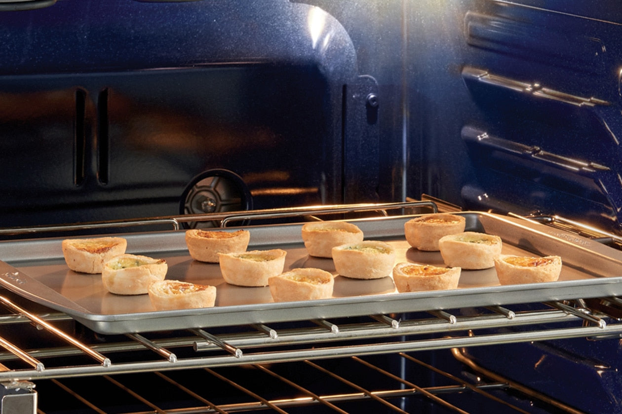 Small savory pies baking on a tray inside a blue interior electric double wall oven for kitchen appliances