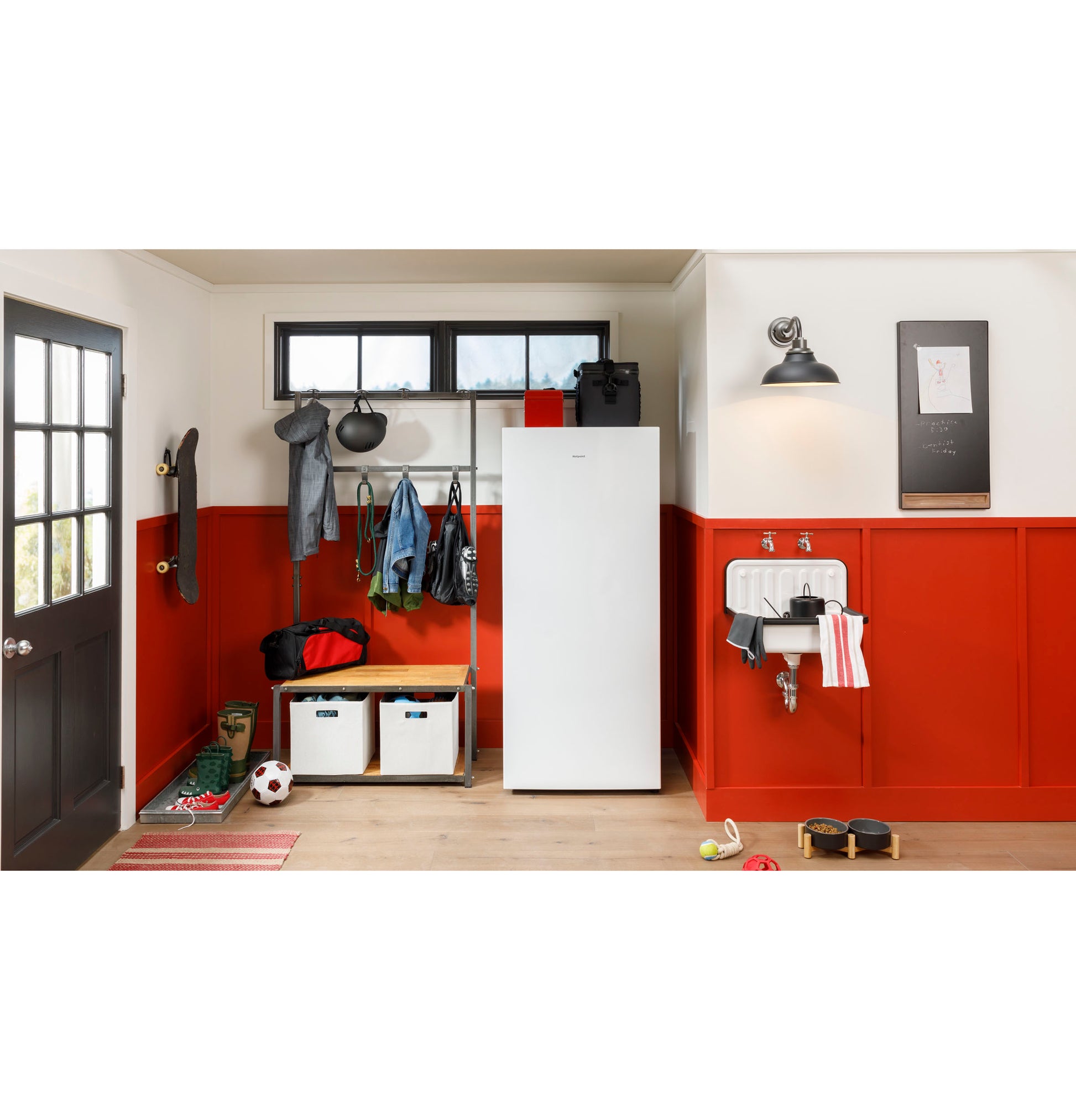 White upright frost-free freezer standing in organized mudroom with red wainscoting and various sports gear nearby