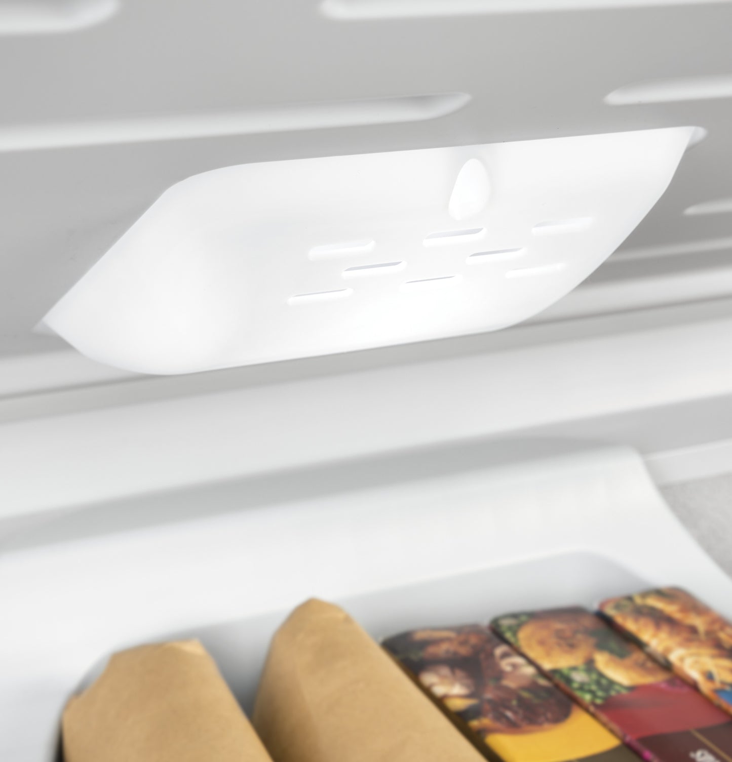 Close-up of interior light fixture above frozen food items inside manual defrost chest freezer in kitchen appliances category