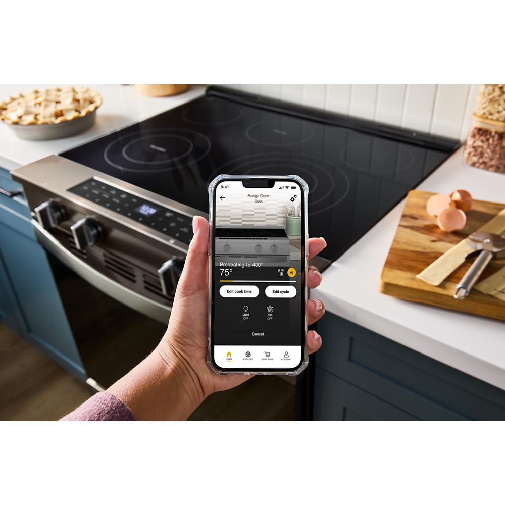 Hand holding smartphone with oven control app in front of 30-inch electric slide-in range on kitchen countertop