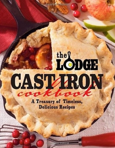 Cast iron skillet with freshly baked fruit pie and cookbook titled Lodge Logic Cast Iron Cookbook nearby