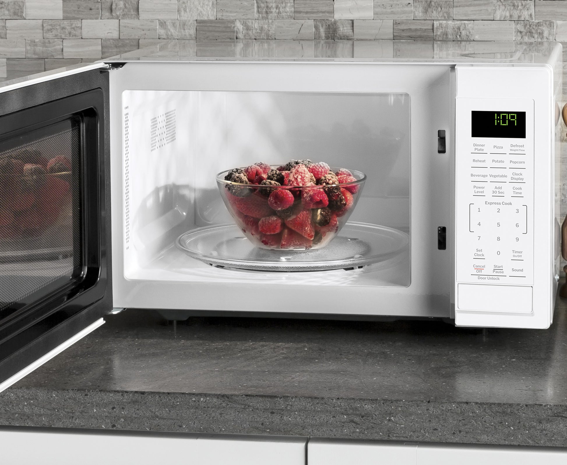 White countertop microwave oven with digital controls and glass bowl of mixed berries inside on kitchen counter