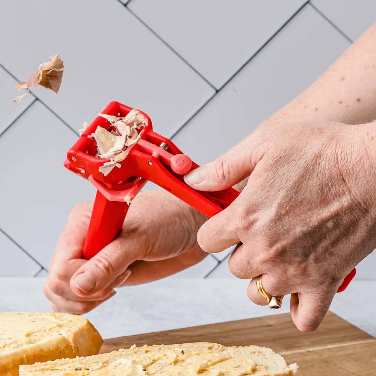 Red garlic press ejecting garlic peel while crushing over bread in kitchenware and cooking utensil collections