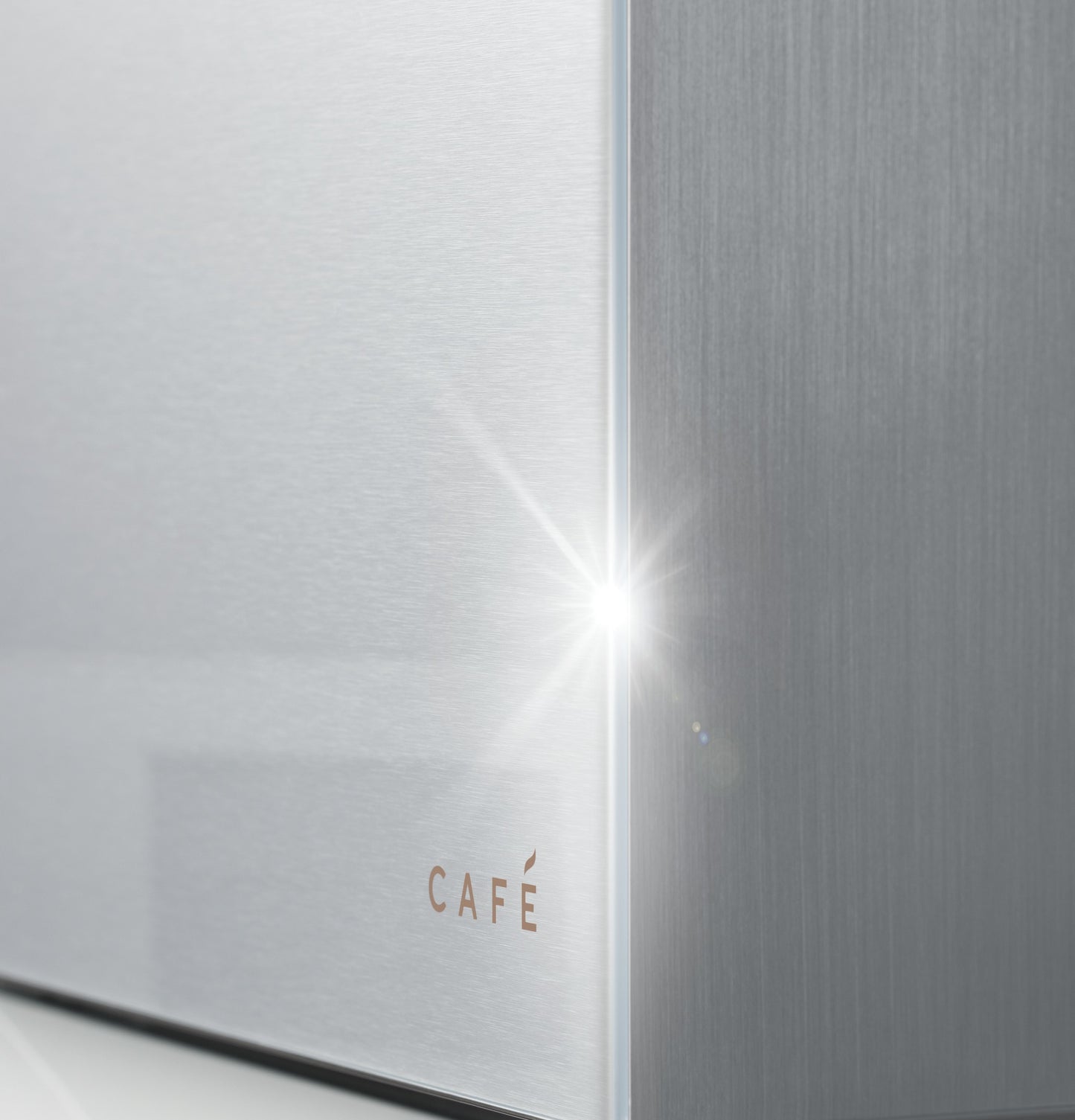 Close-up of platinum glass and stainless steel corner with subtle CAFÉ logo in modern kitchen appliance collection