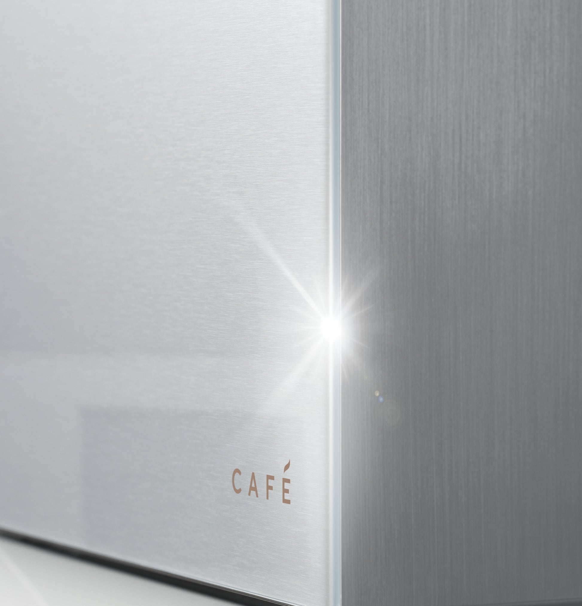 Close-up of platinum glass and stainless steel corner with subtle CAFÉ logo in modern kitchen appliance collection