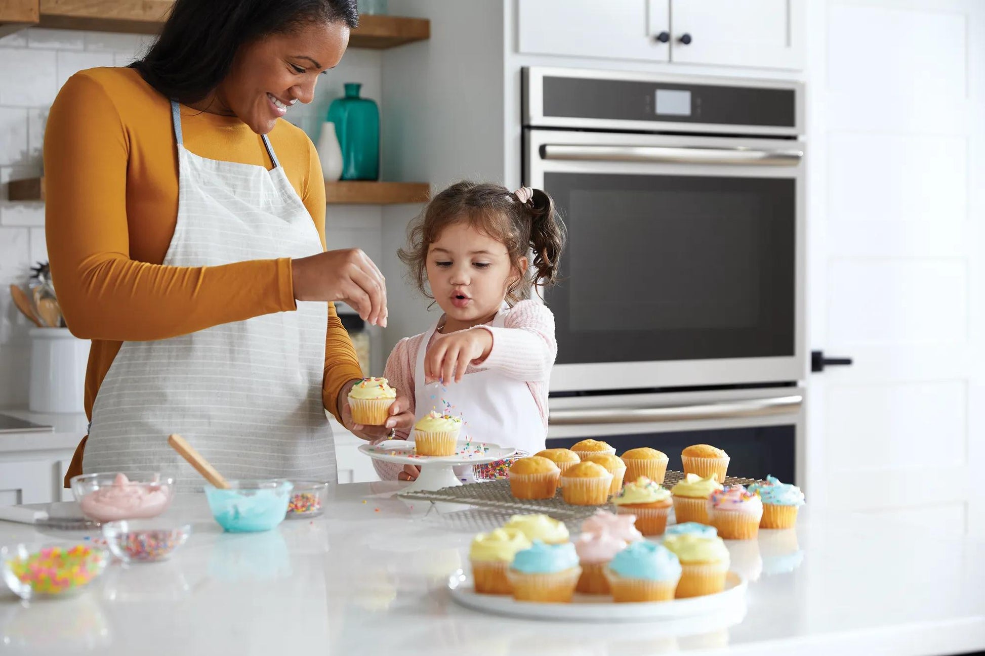 Mother and daughter decorating cupcakes together in a kitchen with stainless steel double electric wall oven from Appliances collection