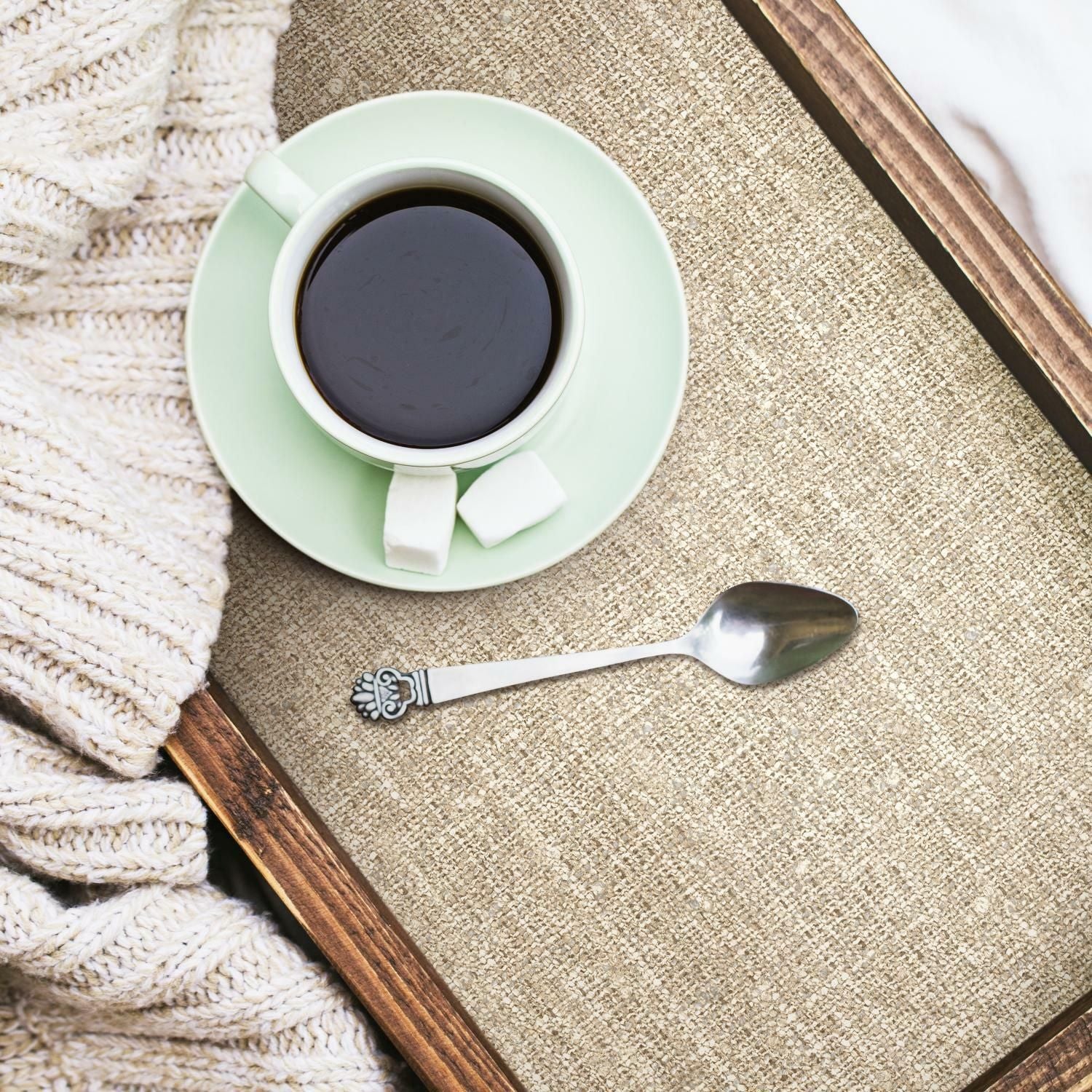Wood tray with brown tweed textured peel and stick wallpaper holding a cup of coffee, sugar cubes, and a silver spoon