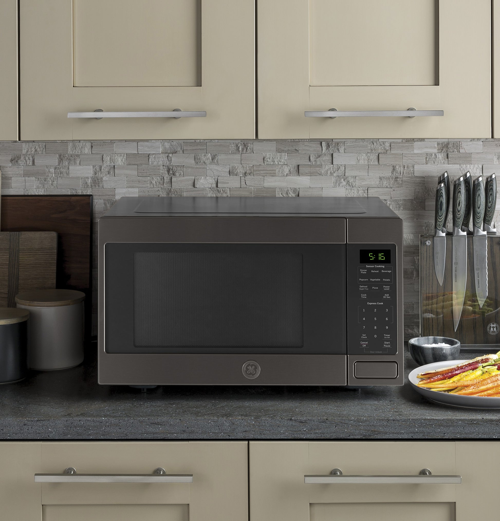 Dark gray countertop microwave with control panel and digital display on kitchen counter with knives and plate nearby
