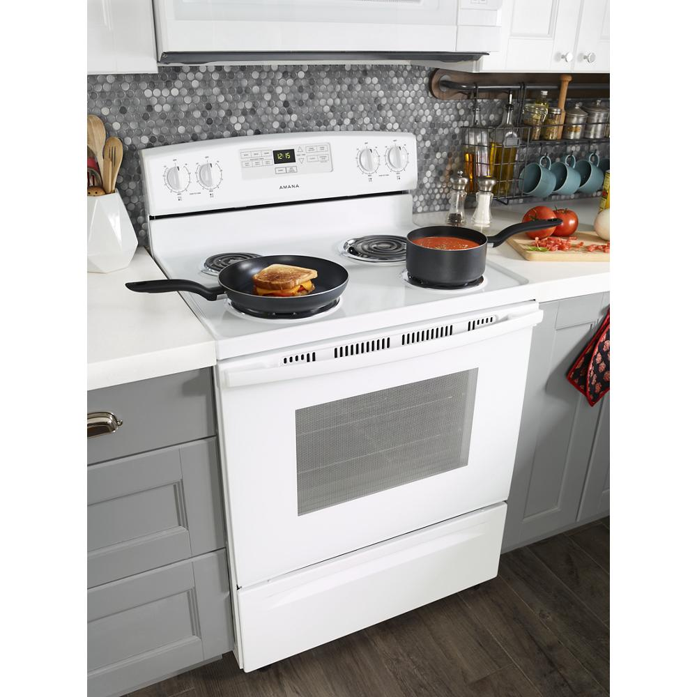 White electric range with coil burners cooking grilled sandwich and sauce in modern kitchen setting
