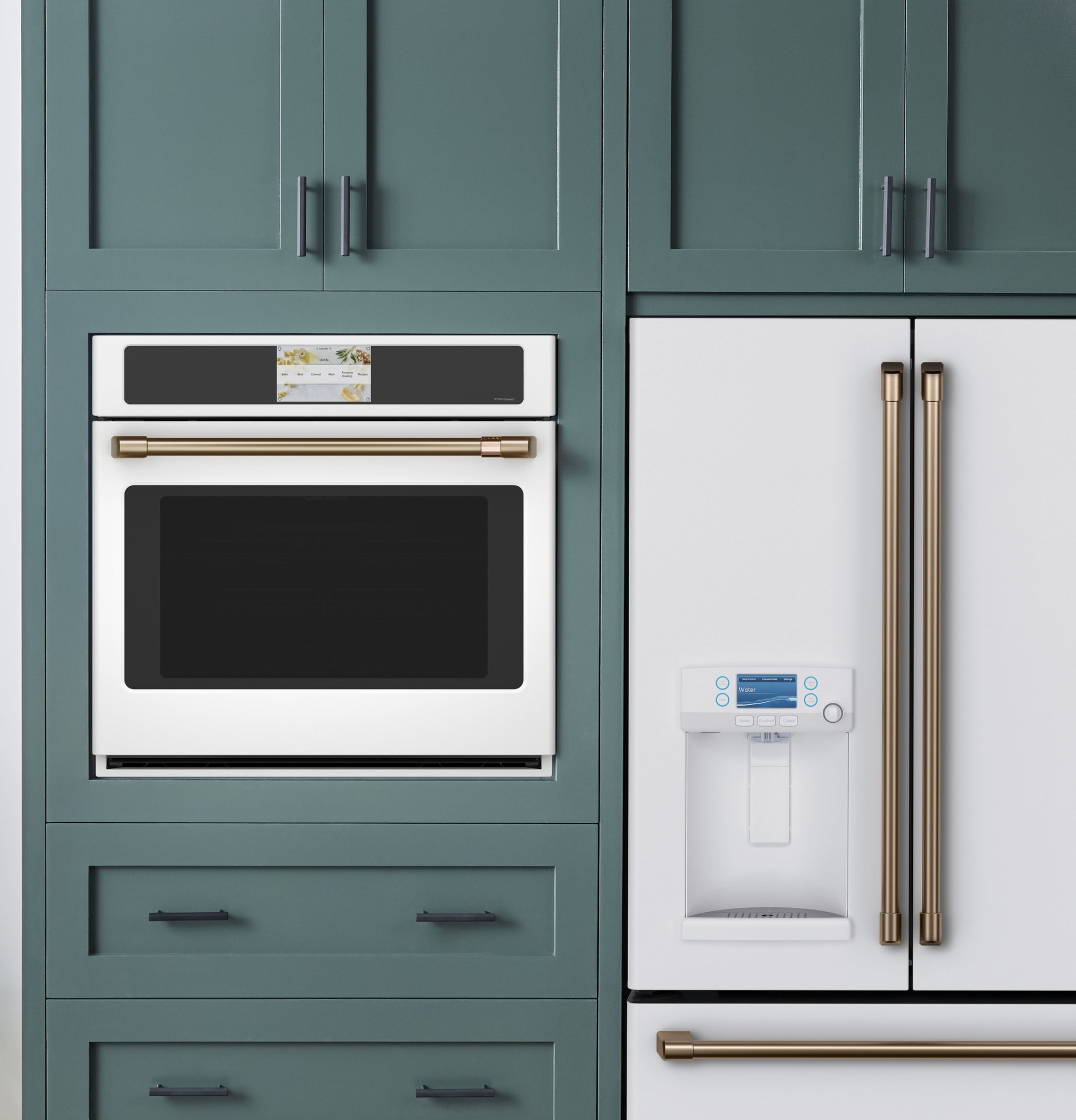 White built-in convection wall oven with touchscreen and brass handle integrated into green kitchen cabinetry next to matching refrigerator
