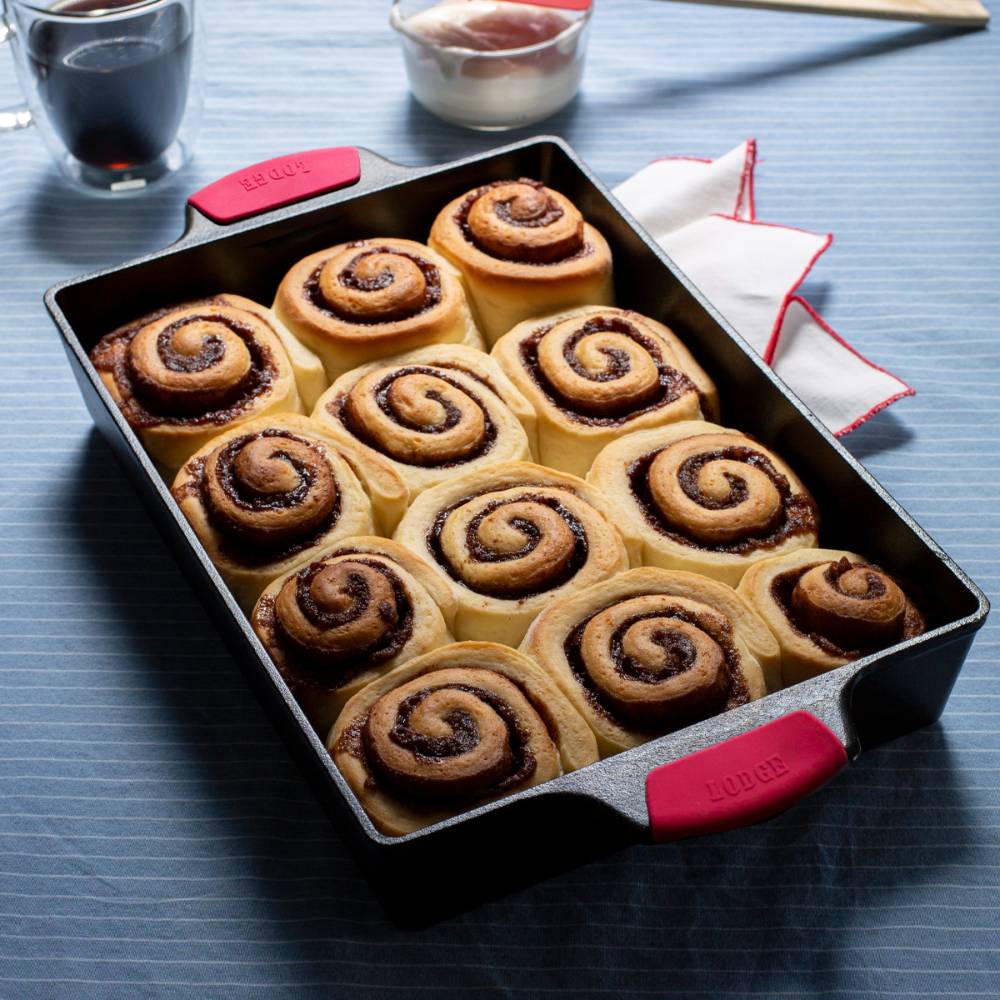 Black cast iron casserole pan with red silicone grips holding a dozen freshly baked cinnamon rolls in kitchenware collections