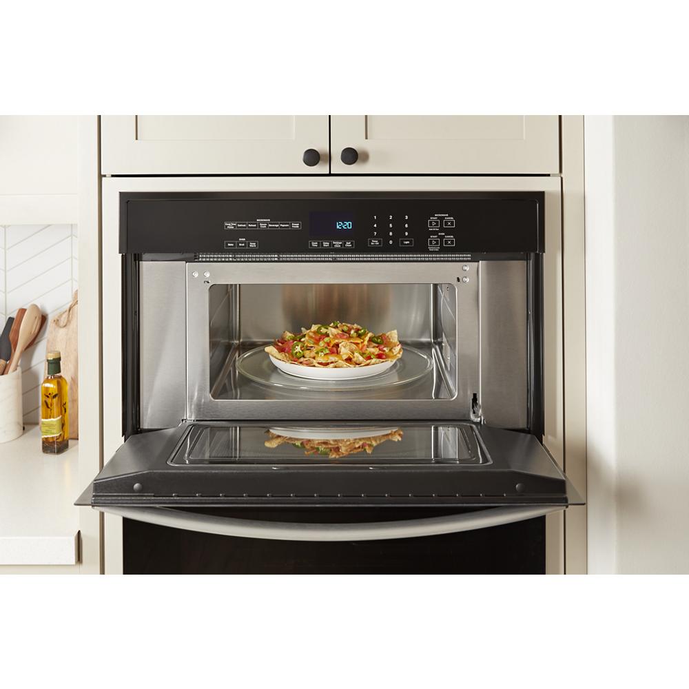Open microwave with black and stainless steel trim cooking a plate of food in a built-in kitchen appliance setting