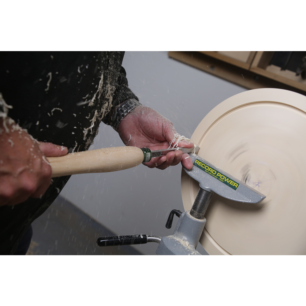 Hands using a sharp woodworking tool with a beech handle on a spinning wood lathe in a workshop setting