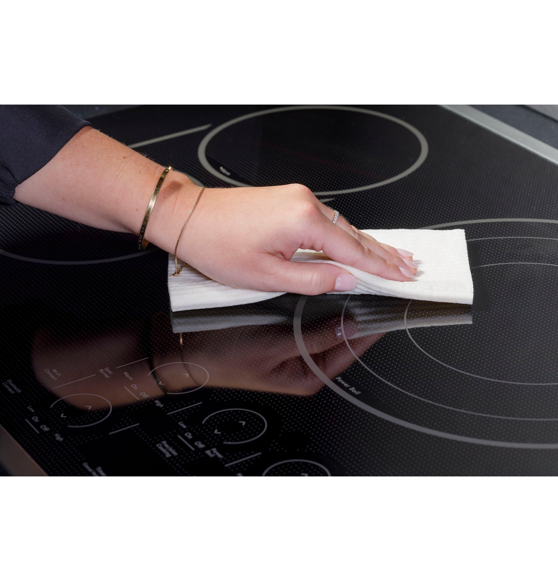 Hand wiping a sleek black glass cooktop with a white cloth in a modern kitchen setting