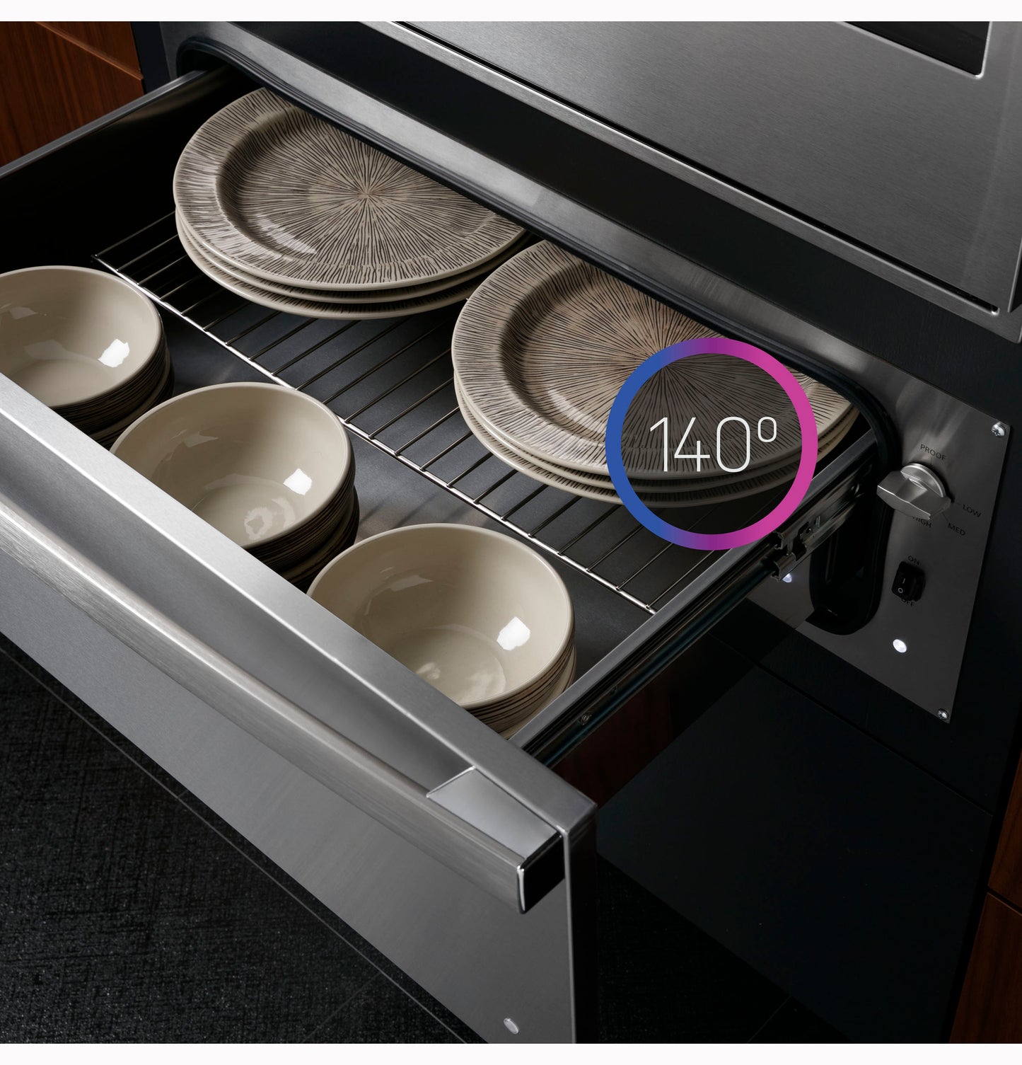 Open stainless steel warming drawer set to 140 degrees warming plates and bowls in a modern kitchen with wood cabinetry
