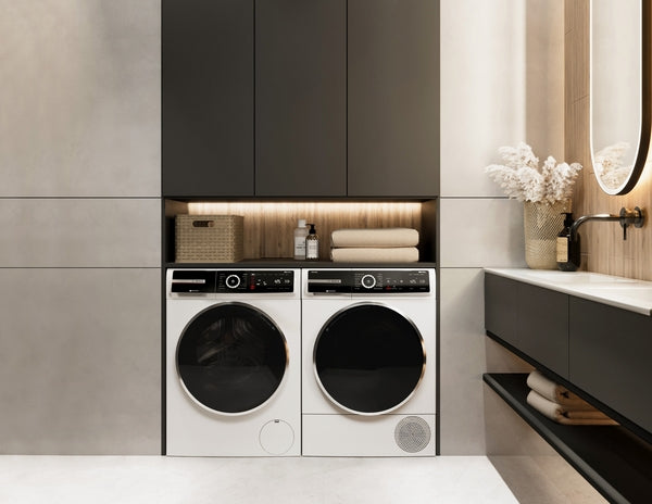 Modern laundry nook with white front load washer and dryer under built-in dark cabinetry and warm lighting accents