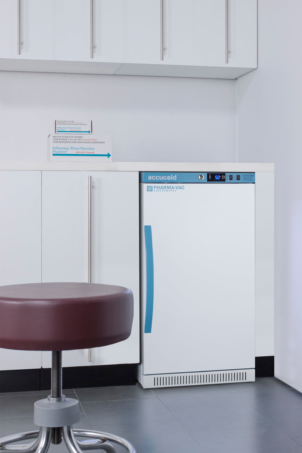 Compact white vaccine refrigerator with blue handle and digital control panel in clinical kitchen appliance setting