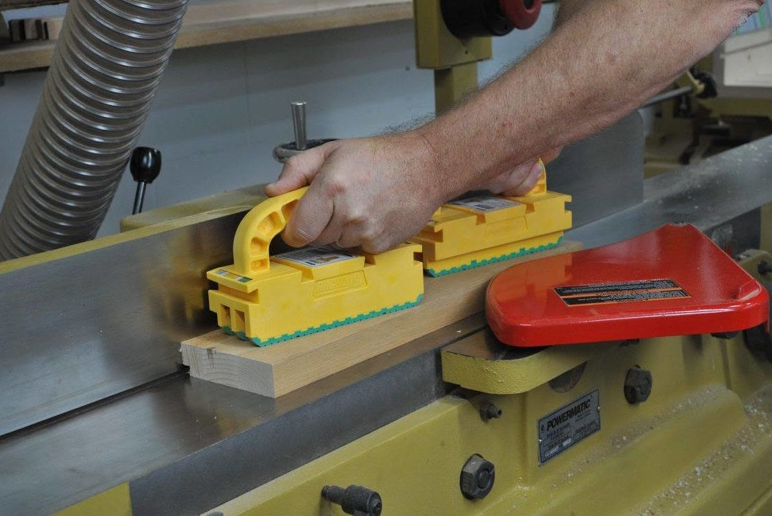 Hand using yellow push block to guide wood for precise and safe cutting in tool accessories and home improvement tools collections