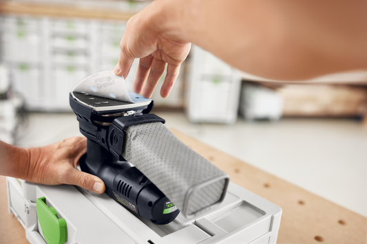 Hand placing gray Festool Granat abrasive sheet onto compact power sander in workshop for home improvement tools