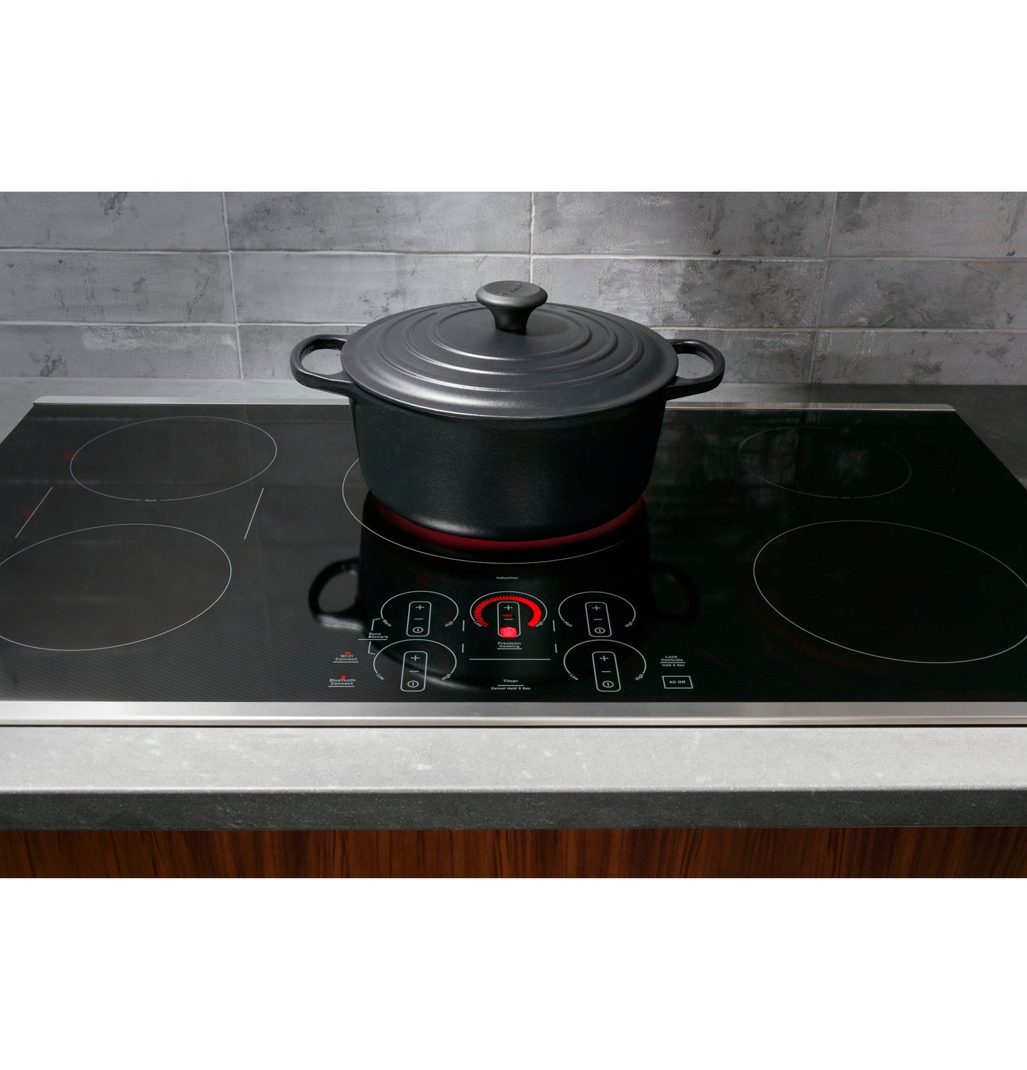 Black induction cooktop with touch controls heating a covered black pot on gray kitchen countertop and tiled backsplash