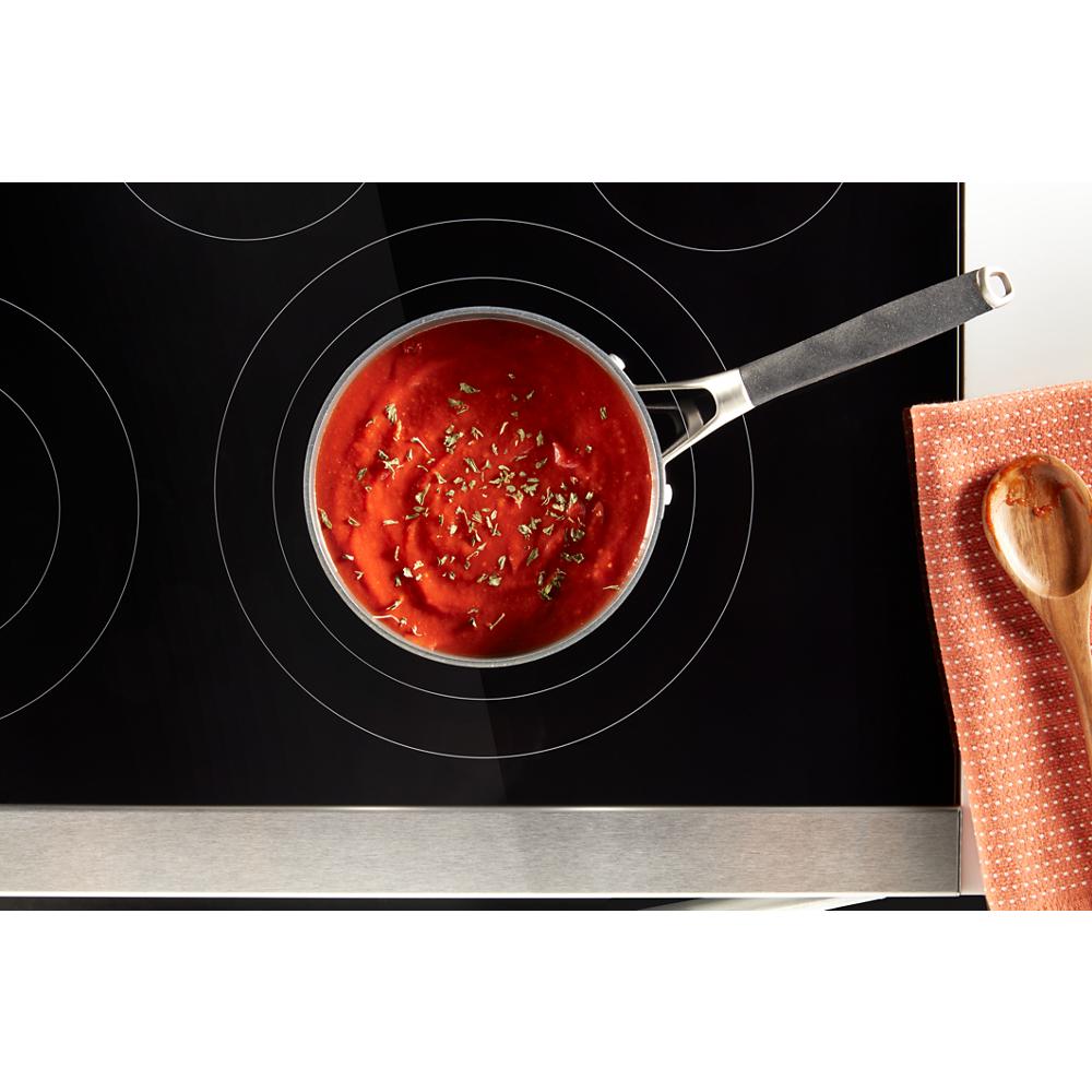 Top-down view of saucepan with tomato sauce and herbs simmering on black induction cooktop in kitchen setting
