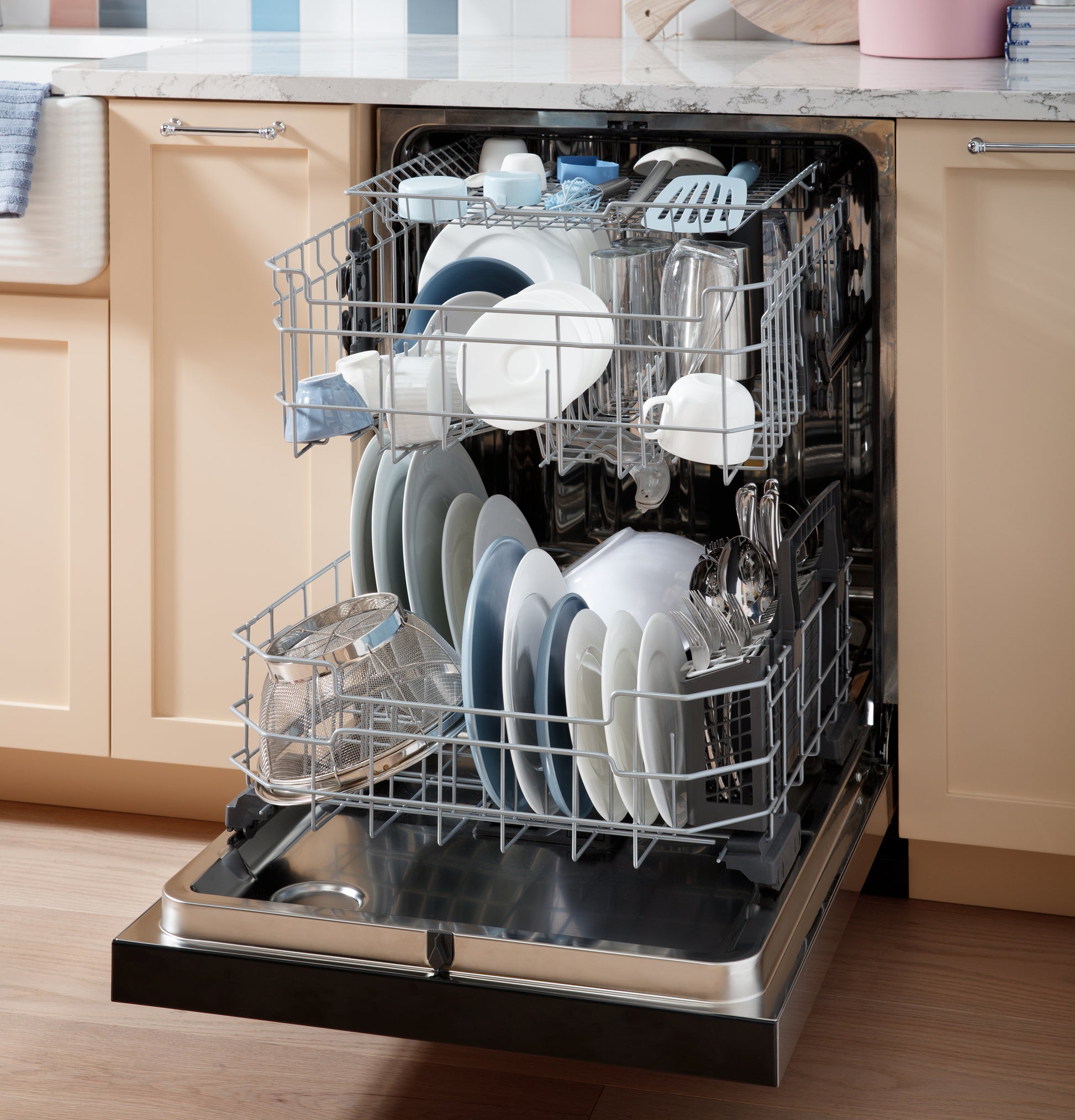 Open stainless steel interior dishwasher with two racks loaded with clean dishes in a kitchen setting