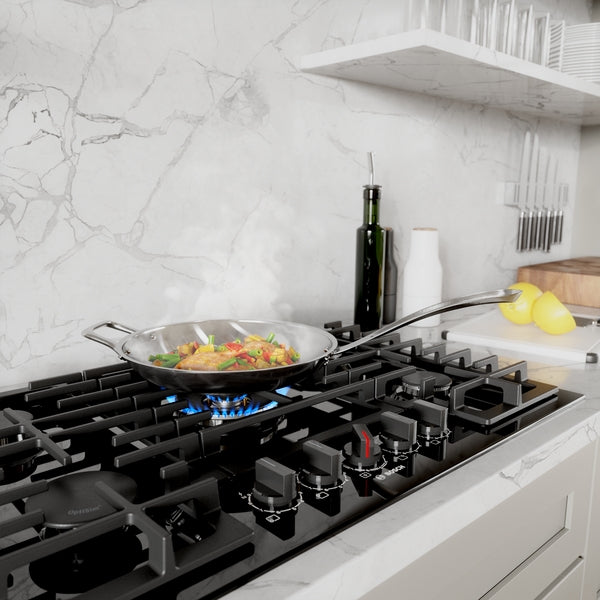 Black gas cooktop with five burners in modern kitchen setting preparing food in stainless steel skillet with olive oil bottle nearby