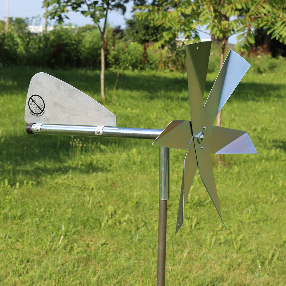 Metal mole deterrent windmill with angled blades and tail vane mounted on pole in grassy garden setting for pest control