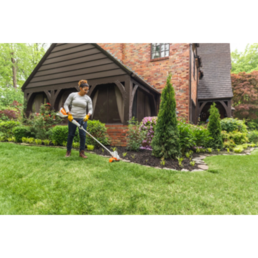 Person trimming grass beside landscaped garden bed using orange and white cordless battery grass trimmer tool