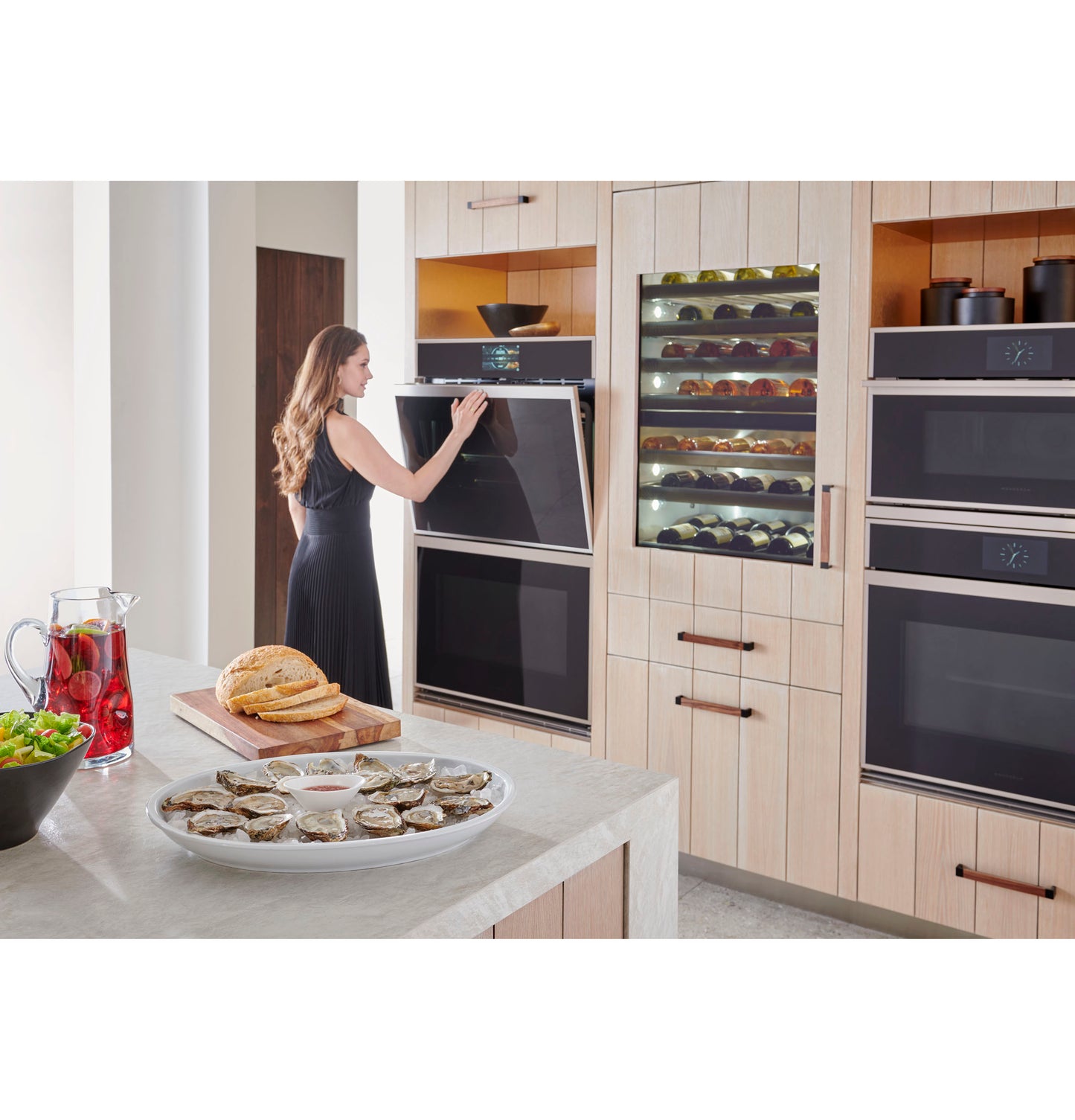 Woman opening lower oven in modern kitchen featuring minimalist double wall ovens and wine cooler in appliances collection