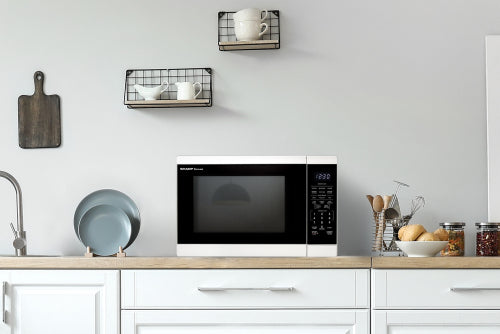 Compact white microwave oven with digital control panel on kitchen counter surrounded by dishes and jars in modern space