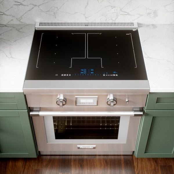 Stainless steel induction professional range with digital controls and dual knobs set in green kitchen cabinetry.