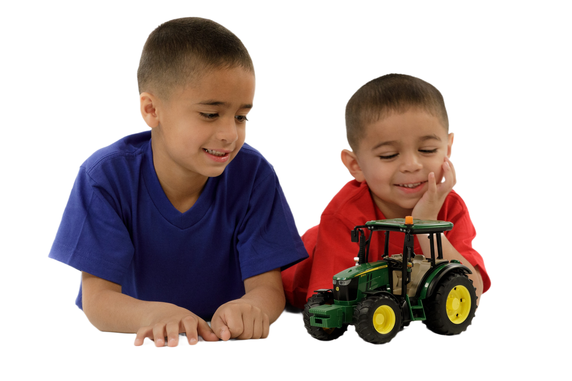 Two young boys smiling and playing with a green and yellow Bruder John Deere 5115 M tractor model toy