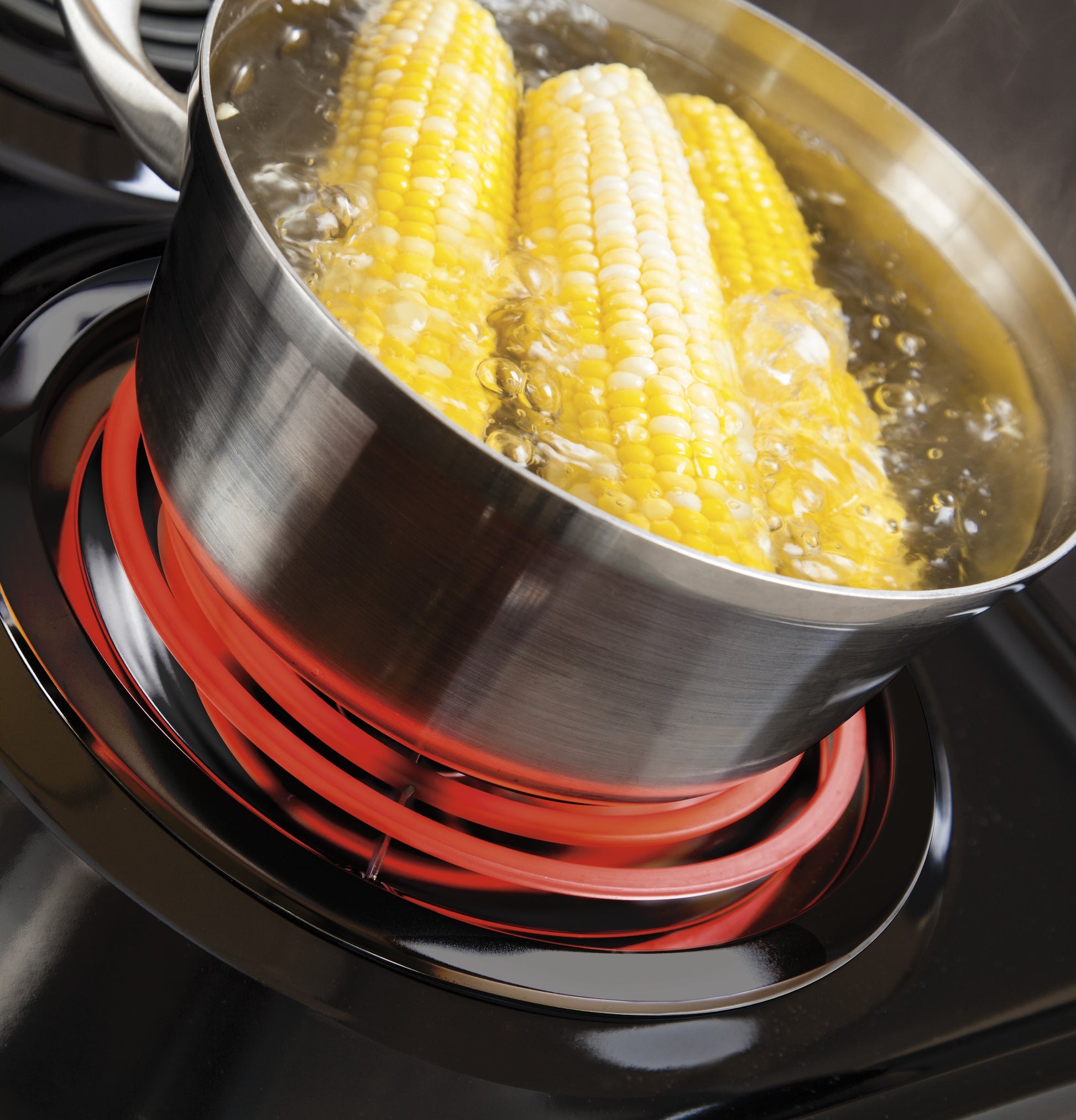 Stainless steel pot boiling corn on the cob on a glowing electric coil burner in kitchen appliance setting