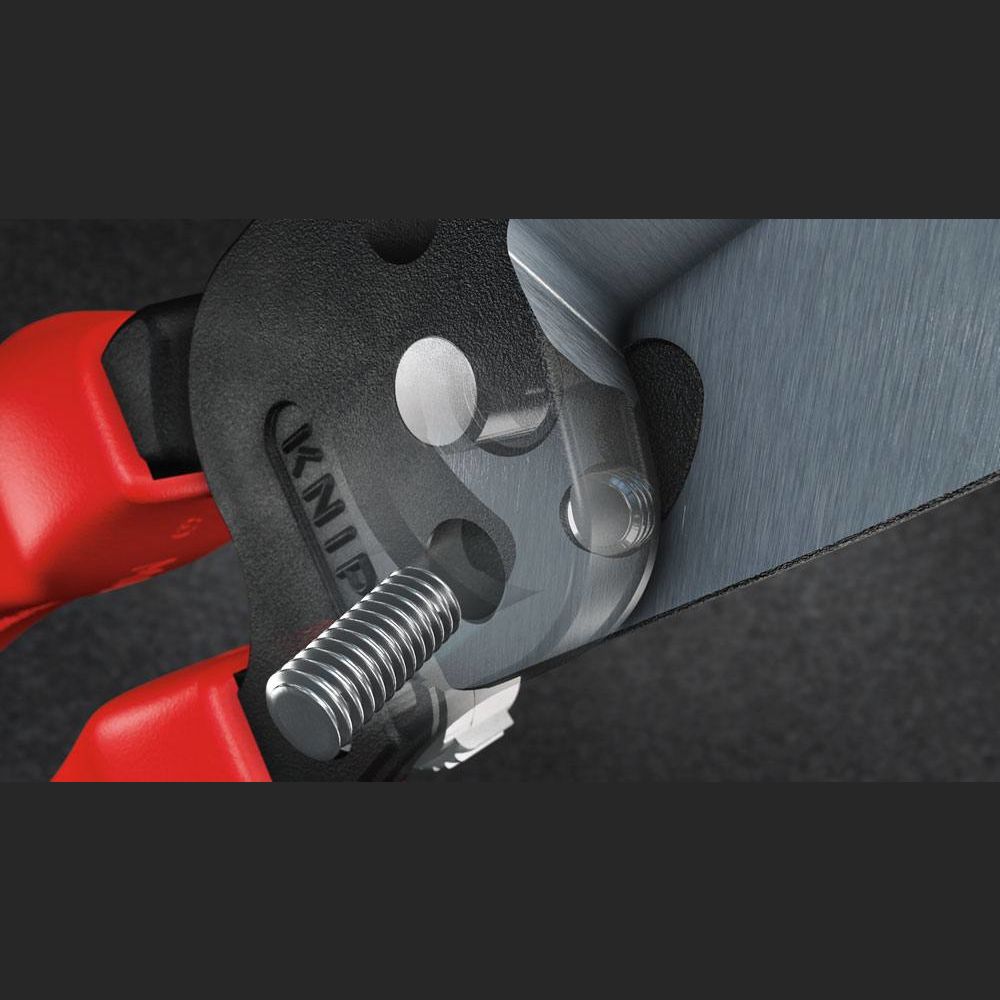 Close-up of KNIPEX forged wire strippers cutting a metallic screw with red ergonomic handles for home improvement tasks