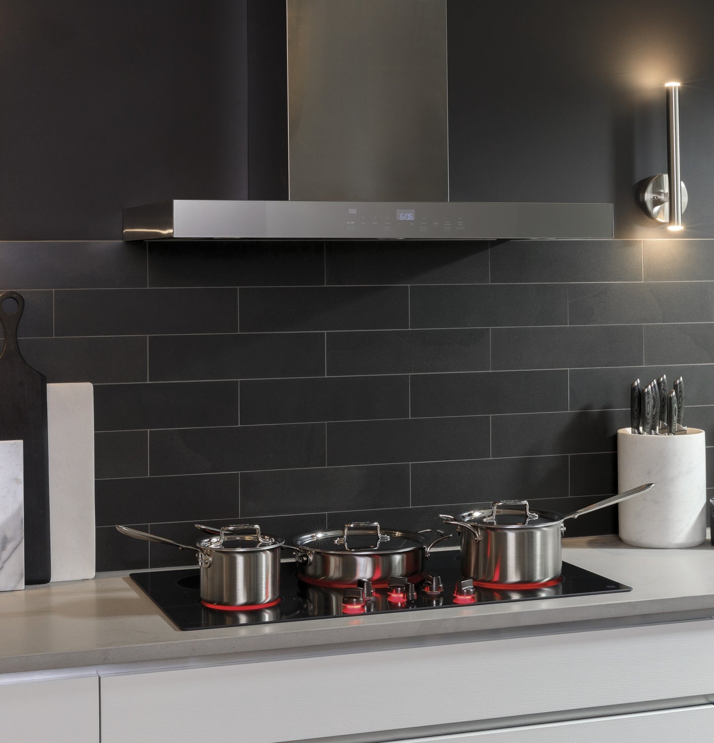 Stainless steel wall mount range hood with perimeter venting above modern gas cooktop in kitchen setting