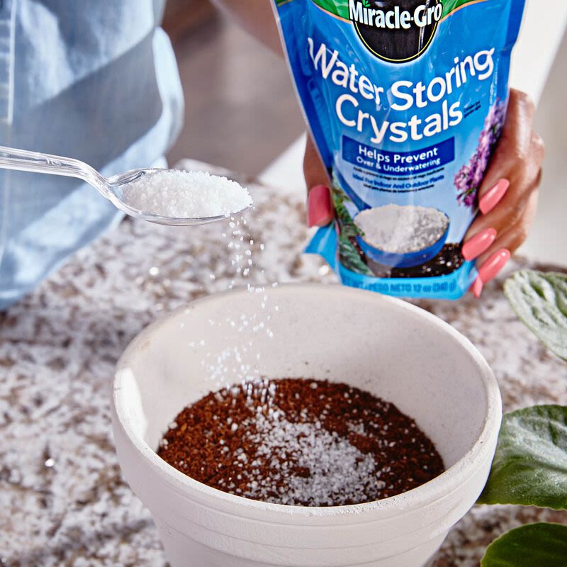 Hand sprinkling white water storing crystals into a white planter with soil for home gardening use