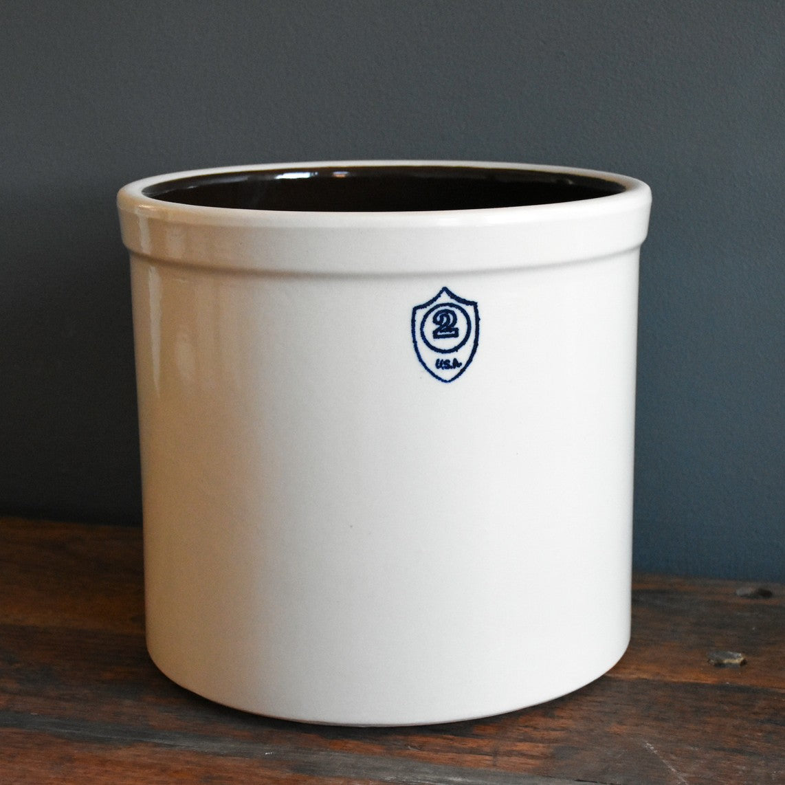 Cream-colored stoneware crock with dark interior and small blue shield emblem marked 2 USA on front