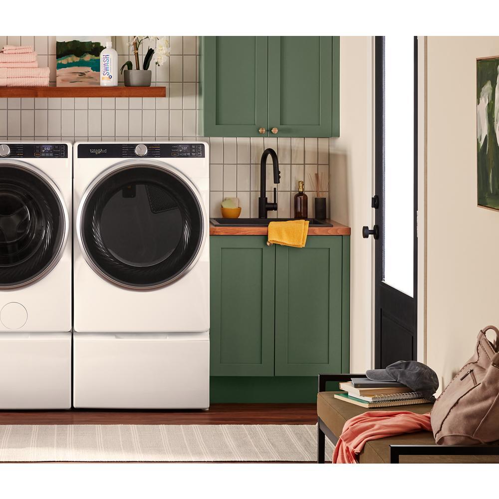 White smart front load electric dryer and washer with digital controls in laundry room with green cabinets and wood countertop
