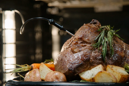 Roast beef with fresh herbs, potatoes, and carrots cooking in a professional kitchen oven setting