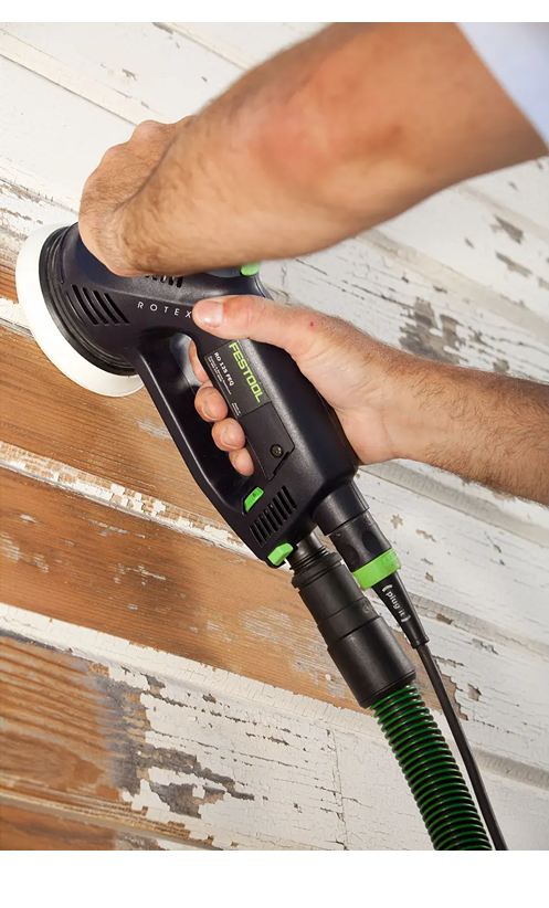 Person sanding peeling paint from weathered wood siding using green and black Festool dual mode power sander for home improvement