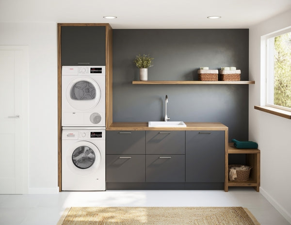 Laundry area with stacked white washer and compact condensation dryer set in gray cabinetry with wood countertop and open shelving