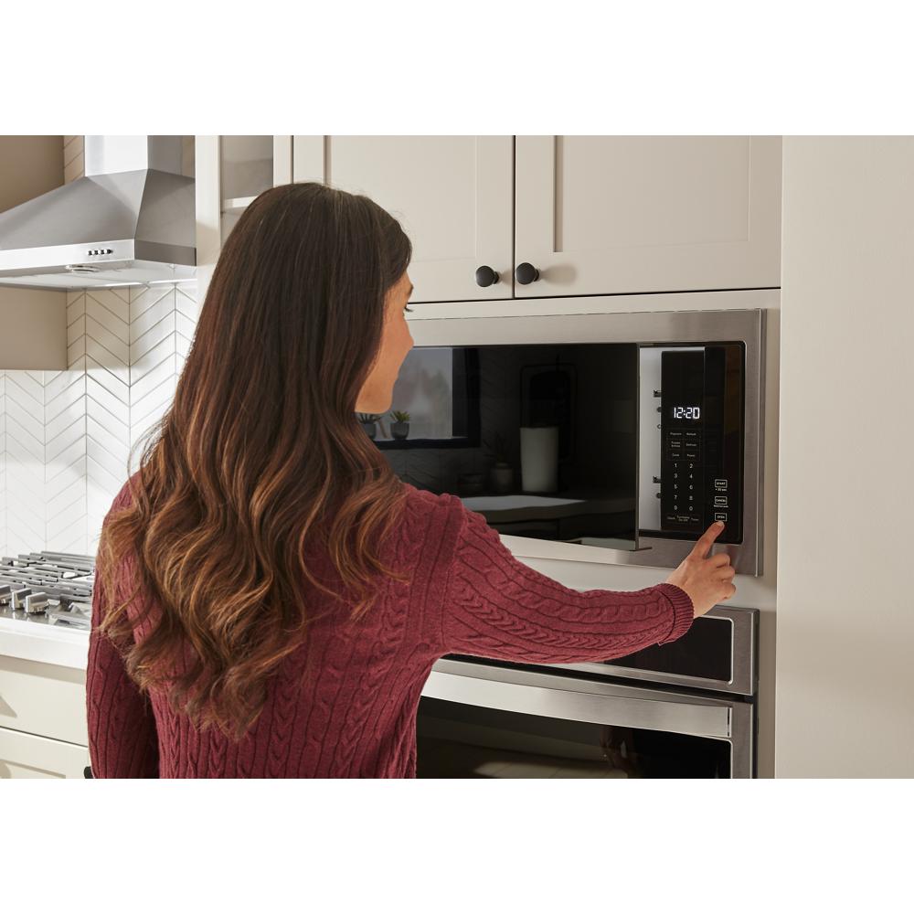 Woman setting a built-in microwave with slim trim in modern kitchen cabinetry from Kitchen & Kitchenware collection