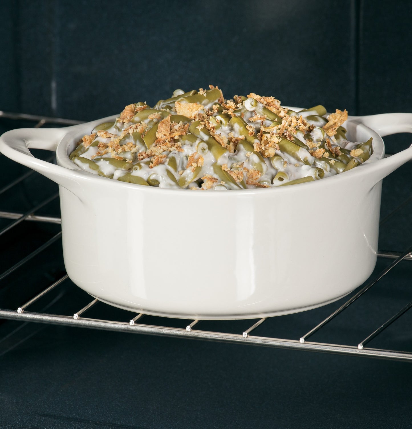 White ceramic casserole dish with green bean casserole baking inside a modern electric range oven